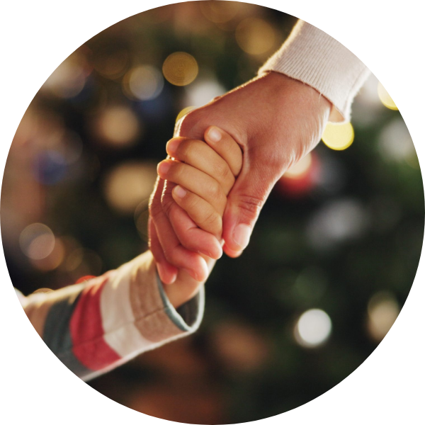 Parent and child holding hands in front of a Christmas tree.