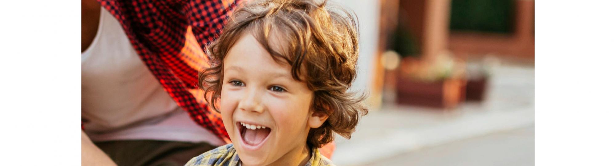 Boy riding bike and smiling while his father is supporting him.