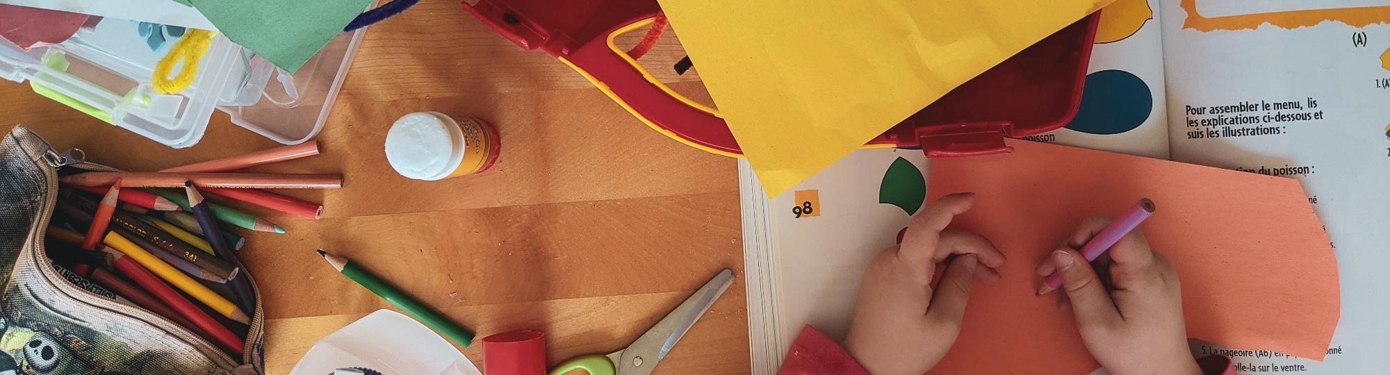 Child drawing with a colored pencil surrounded by crafting items.